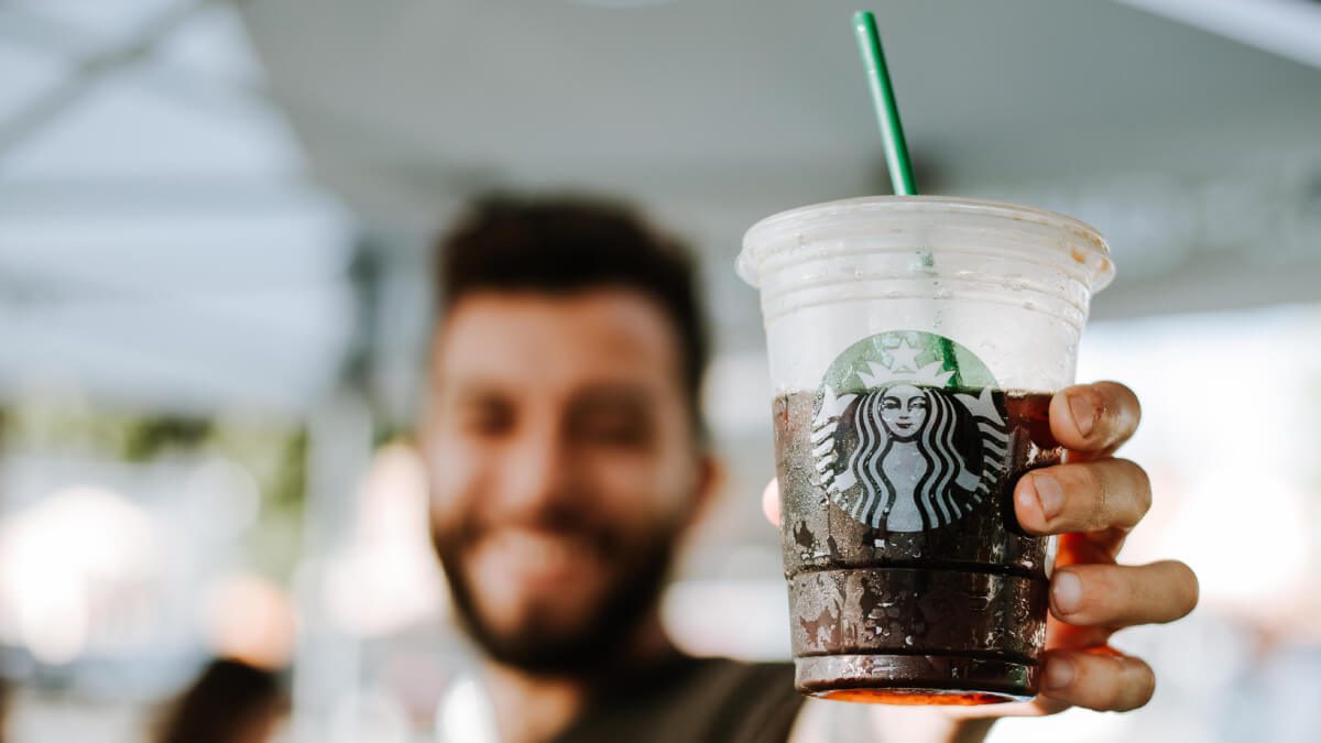 bearded man holding starbucks iced coffee in the summer