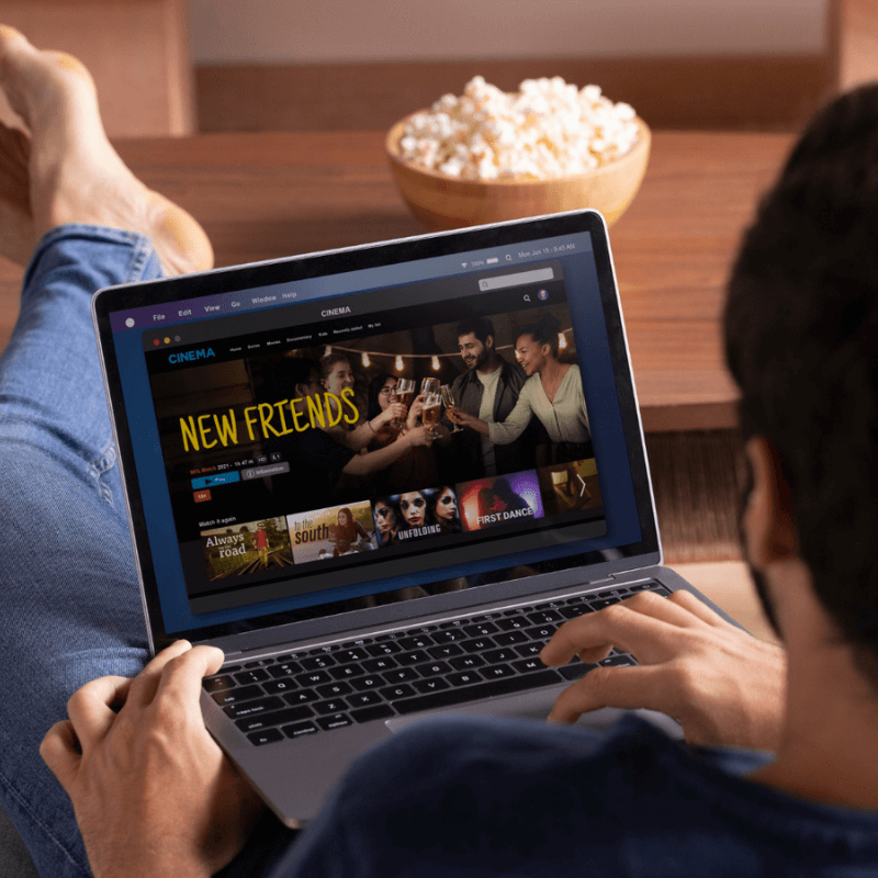 guy browsing moview on laptop in his lap, pop corn ready on the table