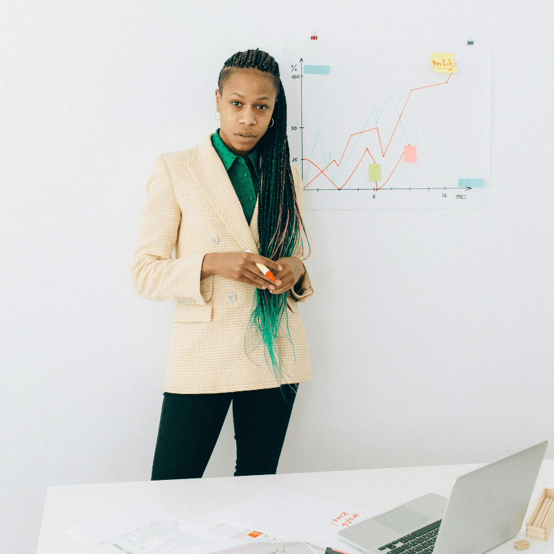 african-american woman in white coast standing with chart on the wall laptop on desk